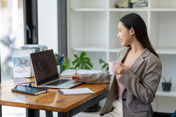 Young adult Asian women work at home or modern office, using a notebook laptop computer. Work from home life, information technology, domestic lifestyle, or self-isolation working concept