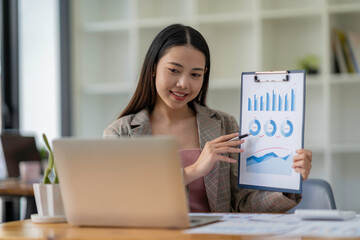 Asian businesswoman working online with laptop computer while Showing graphs to colleagues in an...