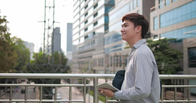 Portrait of happy Asian businessman walking on the skywalk in the modern city with building background at outdoor.