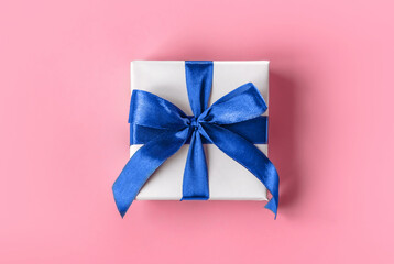 Banner of Gift wrapped in white paper with a blue bow made of satin on on soft pink background. St Valentines day, Birthday, New Year, Christmas, Mothers or Fathers day presents concept