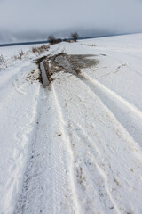 Snowy road in a field leading to pine forest. Winter road to nowhere in sunny day, snow-covered fresh car track. Car traces in a deep snow of remote rural area