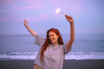 Joyful young woman celebrating with bengal lights at the beach