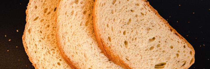 slices of white bread close up on a black background. rough dappled textured surface chopped pieces loaf of natural organic food with holes. top view. banner