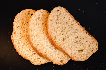 slices of white bread close up on a black background. rough dappled textured surface chopped pieces loaf of natural organic food with holes. top view