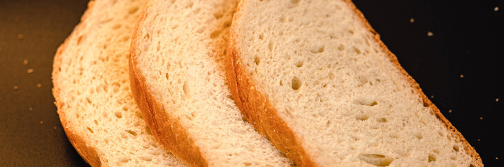 slices of white bread close up on a black background. rough dappled textured surface chopped pieces loaf of natural organic food with holes. banner