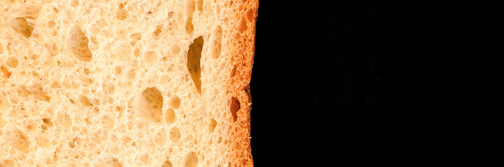 slice of white bread close up isolated on a black background. rough textured surface chopped piece...