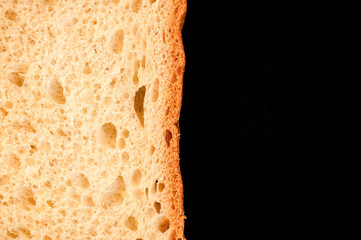 slice of white bread close up isolated on a black background. rough dappled textured surface...