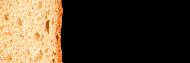 slice of white bread close up isolated on a black background. rough textured surface chopped piece loaf of natural organic food with holes. top view. abstract concept of the planet and space. banner