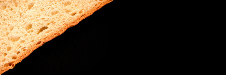 slice of white bread close up isolated on a black background. rough textured surface chopped piece loaf of natural organic food with holes. top view. abstract concept of the planet and space. banner