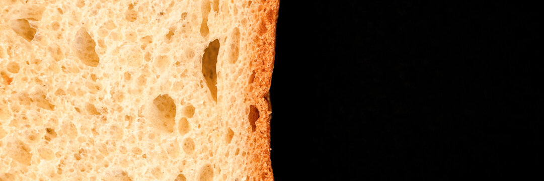 slice of white bread close up isolated on a black background. rough textured surface chopped piece loaf of natural organic food with holes. top view. abstract concept of the planet and space. banner