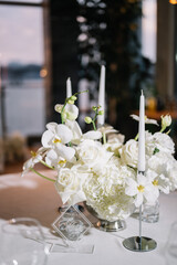 Stylish decoration of a wedding dinner in a classic bohemian style with white tablecloths and vases with white flowers