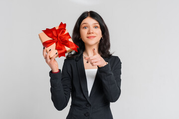 Fototapeta premium Curious cute brunette teenager girl in black blazer celebrating birthday, wonder whats inside b-day gift, shaking box and smiling happy, white background. Holidays, celebration and birthday concept