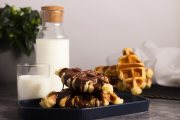 Freshly made Croffle waffles drizzled with rich chocolate sauce, paired with milk on a neutral...