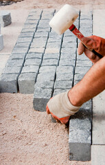 Construction worker laying stone cobbles  in sand - 496285883