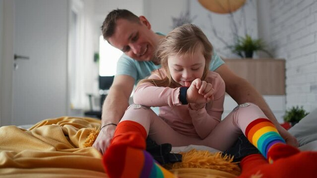Father with his little daughter with Down syndrome sitting on bed and bonding at home.