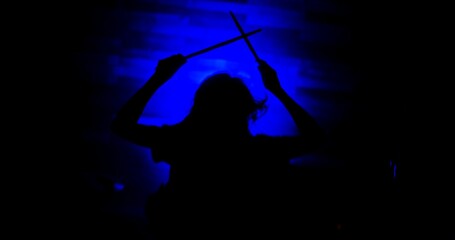 Silhouette of female drummer holding drum sticks up in the air during a show