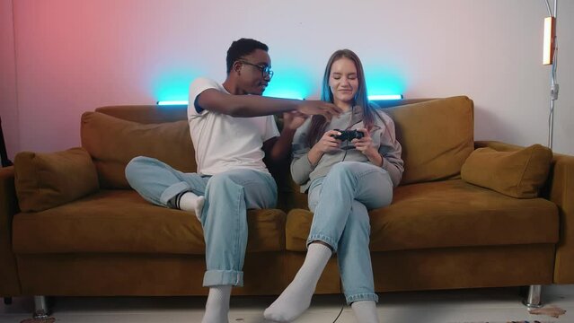 A young girl plays a console and a young african american guy take away the joystick from her and the dog watches how they fight jokingly