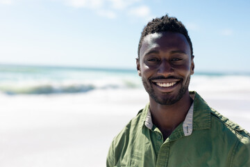 Portrait of happy african american man standing at beach enjoying sunny day