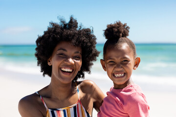 Portrait of happy african american mother and daughter enjoying sunny day at beach