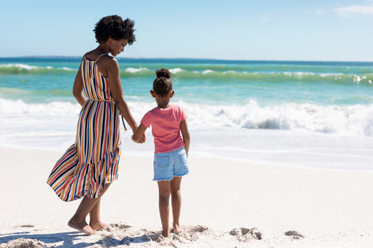 Full Length Rear View Of African American Mother And Daughter Holding Hands While Standing At Beach