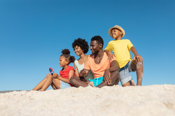 Happy african american family on sand at beach against clear blue sky with copy space