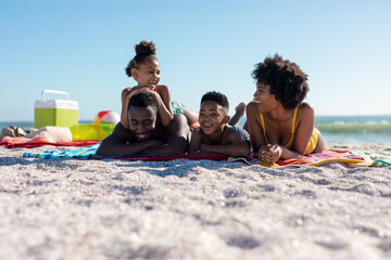 Happy african american family lying on towel while relaxing at beach on sunny day