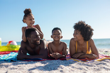 Portrait of smiling african american boy lying with family on towel at beach during sunny day