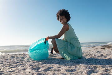 Side view portrait of smiling african american crouching with plastic bag while collecting waste
