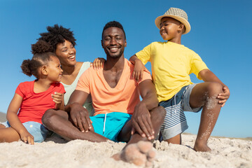 Fototapeta premium Portrait of happy african american parents and children on sand at beach against blue sky
