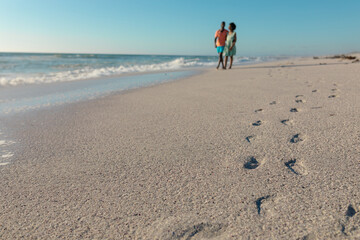Footprints on sand at beach with african american couple walking during sunny day