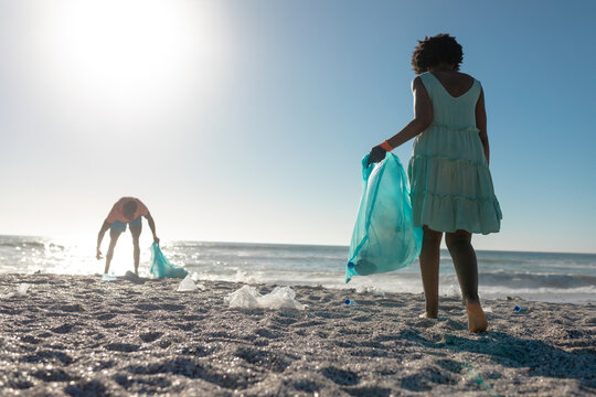 Full length of african american couple picking waste on sand at beach against clear blue sky