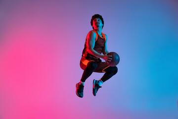 Fototapeta na wymiar Young energetic man playing basketball isolated on gradient pink blue studio background in neon light. Youth, hobby, motion, activity, sport concepts.
