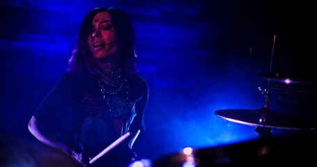 Fototapeta na wymiar Portrait of Professional female drummer playing drums in twinkling blue lights