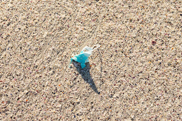 Directly above view of abandoned protective face mask in white sand at beach during sunny day