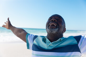 Happy african american senior retired man with eyes closed and arms outstretched at beach