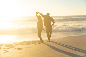 Happy african american senior couple dancing on shore at beach during sunset