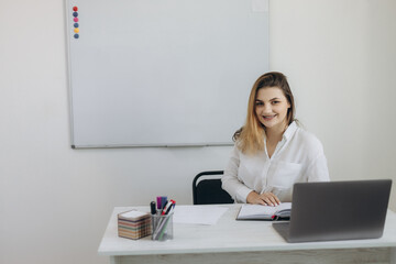 Portrait of a beautiful young teacher conducting online learning in the classroom for her students. The girl is dressed in a white shirt. She looks at the camera