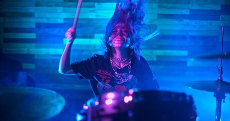 Drummer girl energetically playing the drums in blue, red and green lights.