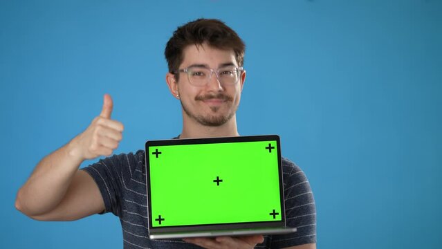 Young smiling happy man 20s wear striped t-shirt use work on laptop pc computer with tracking points green screen, browsing chatting with blank screen workspace area isolated on solid blue background