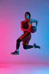 Fototapeta na wymiar Sportive man playing basketball isolated on gradient pink blue studio background in neon light. Youth, hobby, motion, activity, sport concepts.