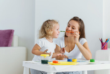 Obraz na płótnie Canvas Mother and toddler daughter painting at home. Happy creative family with child spending time together with fun and joy. Learning colours