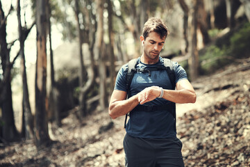 Checking his time. Cropped shot of a handsome young man checking his watch while out hiking in the...
