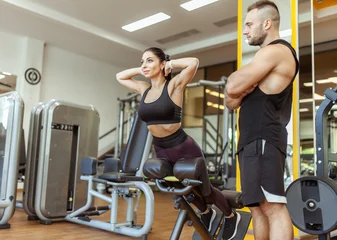 Tuinposter Young fit woman training muscles with personal trainer man in the gym © splitov27
