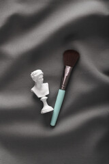 Venus bust with makeup brush on gray fabric background
