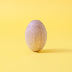 Minimal composition with wooden egg on pastel yellow background.