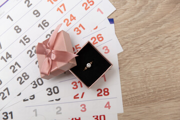 Engagement ring in gift box and calendar on table