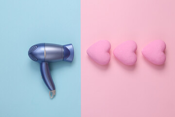 Hair dryer and hearts on pink blue background. Love concept. Top view