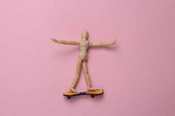 Wooden puppet on skateboard, pink background. Top view