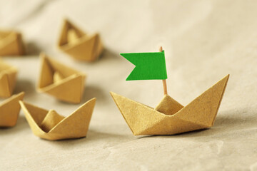 Origami recycled paper boat with green flag leading a group of small boats - Concept of leadership, teamwork and ecology - 496295411