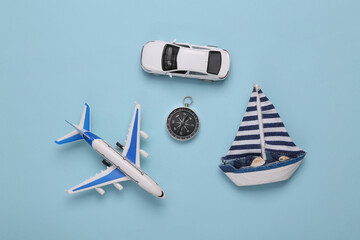 Toy Passenger plane, car and sailboat, compass on blue background. Transport. Travel concept. Top...